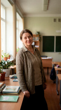 Experienced senior female teacher standing in traditional classroom by sunlit window