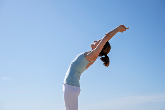 woman doing a back stretch exercise outdoors under a blue sky