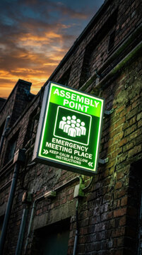 Glowing Assembly Point Sign Lit Against Dramatic Sunset Sky
