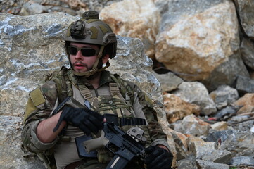 Obraz premium Focused military infantry soldier lying prone on rugged rocky terrain aiming a tactical assault rifle during a dangerous combat training mission for national defense and special security.