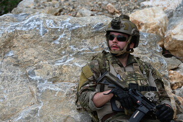 Obraz premium Focused military infantry soldier lying prone on rugged rocky terrain aiming a tactical assault rifle during a dangerous combat training mission for national defense and special security.
