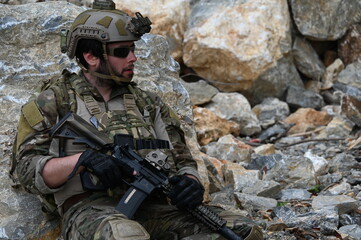 Obraz premium Focused military infantry soldier lying prone on rugged rocky terrain aiming a tactical assault rifle during a dangerous combat training mission for national defense and special security.