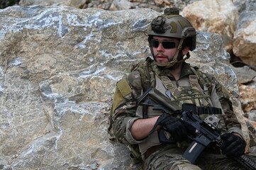 Obraz premium Focused military infantry soldier lying prone on rugged rocky terrain aiming a tactical assault rifle during a dangerous combat training mission for national defense and special security.