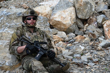 Obraz premium Focused military infantry soldier lying prone on rugged rocky terrain aiming a tactical assault rifle during a dangerous combat training mission for national defense and special security.