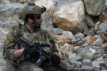 Obraz premium Focused military infantry soldier lying prone on rugged rocky terrain aiming a tactical assault rifle during a dangerous combat training mission for national defense and special security.