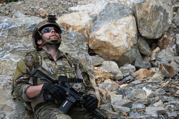 Obraz premium Focused military infantry soldier lying prone on rugged rocky terrain aiming a tactical assault rifle during a dangerous combat training mission for national defense and special security.