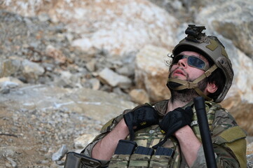 Obraz premium Focused military infantry soldier lying prone on rugged rocky terrain aiming a tactical assault rifle during a dangerous combat training mission for national defense and special security.