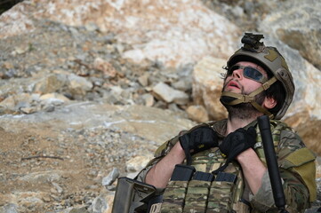 Obraz premium Focused military infantry soldier lying prone on rugged rocky terrain aiming a tactical assault rifle during a dangerous combat training mission for national defense and special security.