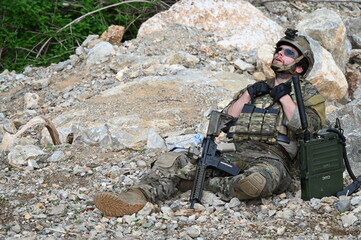 Obraz premium Focused military infantry soldier lying prone on rugged rocky terrain aiming a tactical assault rifle during a dangerous combat training mission for national defense and special security.