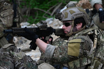 Obraz premium Focused military infantry soldier lying prone on rugged rocky terrain aiming a tactical assault rifle during a dangerous combat training mission for national defense and special security.