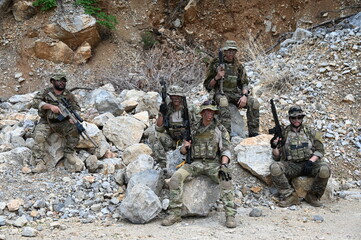Obraz premium Dedicated squad of professional armed military soldiers walking in patrol formation along a rugged rocky mountain cliff during a dangerous tactical combat mission or outdoor training exercise.