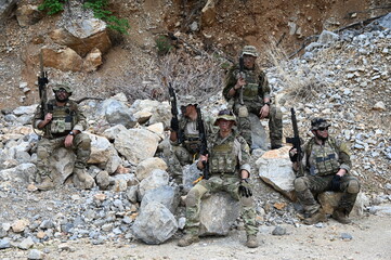 Obraz premium Dedicated squad of professional armed military soldiers walking in patrol formation along a rugged rocky mountain cliff during a dangerous tactical combat mission or outdoor training exercise.