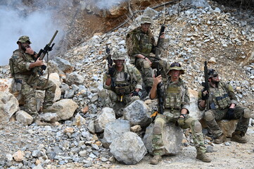 Obraz premium Dedicated squad of professional armed military soldiers walking in patrol formation along a rugged rocky mountain cliff during a dangerous tactical combat mission or outdoor training exercise.