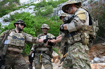 Fototapeta premium Tactical team in camouflage gear checks a navigation device during outdoor training in rocky terrain. Concept of teamwork, communication, security, and field operations.