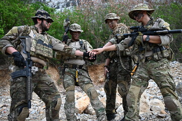 Fototapeta premium Tactical team in camouflage gear checks a navigation device during outdoor training in rocky terrain. Concept of teamwork, communication, security, and field operations.