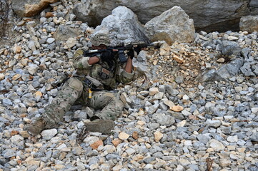 Obraz premium Focused military infantry soldier lying prone on rugged rocky terrain aiming a tactical assault rifle during a dangerous combat training mission for national defense and special security.