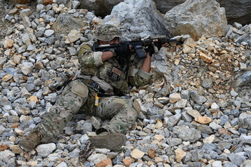 Obraz premium Focused military infantry soldier lying prone on rugged rocky terrain aiming a tactical assault rifle during a dangerous combat training mission for national defense and special security.