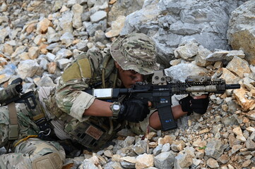 Obraz premium Focused military infantry soldier lying prone on rugged rocky terrain aiming a tactical assault rifle during a dangerous combat training mission for national defense and special security.
