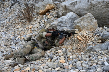 Obraz premium Focused military infantry soldier lying prone on rugged rocky terrain aiming a tactical assault rifle during a dangerous combat training mission for national defense and special security.