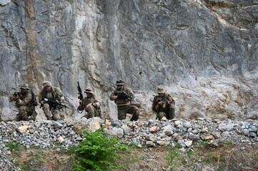 Obraz premium Dedicated squad of professional armed military soldiers walking in patrol formation along a rugged rocky mountain cliff during a dangerous tactical combat mission or outdoor training exercise.