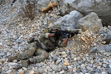 Obraz premium Focused military infantry soldier lying prone on rugged rocky terrain aiming a tactical assault rifle during a dangerous combat training mission for national defense and special security.