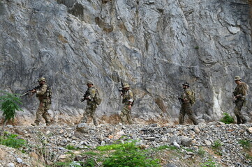 Obraz premium Dedicated squad of professional armed military soldiers walking in patrol formation along a rugged rocky mountain cliff during a dangerous tactical combat mission or outdoor training exercise.