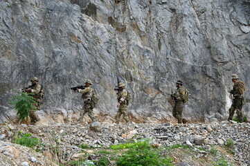 Obraz premium Dedicated squad of professional armed military soldiers walking in patrol formation along a rugged rocky mountain cliff during a dangerous tactical combat mission or outdoor training exercise.