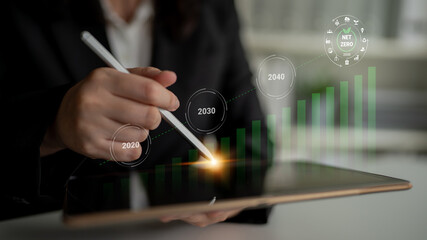 Obraz premium A business professional uses a stylus on a tablet, analyzing growth projections for achieving sustainability and net zero emissions by 2040, symbolizing strategic planning. Gantry