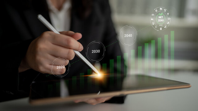 A business professional uses a stylus on a tablet, analyzing growth projections for achieving sustainability and net zero emissions by 2040, symbolizing strategic planning. Gantry