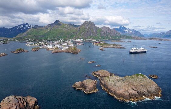 A breathtaking wide aerial panorama captures a luxury cruise ship navigating the deep sapphire waters near Svolv&aelig;r, Norway, surrounded by rugged islands and towering Arctic peaks