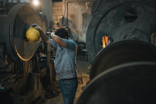 solution production problem shortage risk Industrial worker removing a safety helmet after a demanding shift in a manufacturing factory reflecting workplace stress fatigue and operational challenges