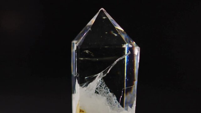 Shifting studio light revealing internal fractures, milky inclusion and chips in clear quartz point