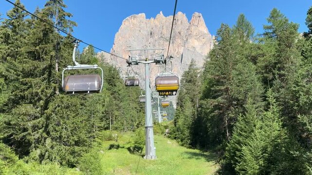 Chairlift ascending through alpine forest beneath Rosengarten peaks, Italy