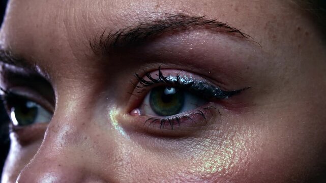 Blinking woman moving right lid in closeup as light glinting, showing glitter eyeliner and mascara