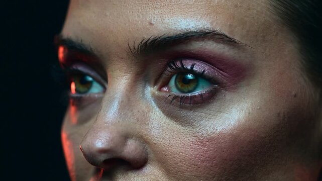 Camera focusing woman blinking and turning gaze in studio, showing shimmery pink eye makeup detail