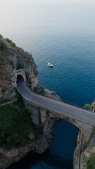 Obraz premium Fiordo di furore bridge and coastal road tunnel connecting rugged cliffs, overlooking the tranquil mediterranean sea with a boat gently floating in the clear blue water, amalfi coast, italy