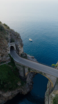 Fiordo di furore bridge and coastal road tunnel connecting rugged cliffs, overlooking the tranquil mediterranean sea with a boat gently floating in the clear blue water, amalfi coast, italy