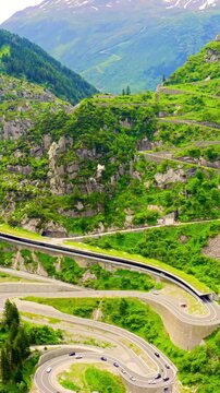Vertical video. Switzerland. View from behind a mountainside on Andermatt. Picturesque winding mountain road with tunnels Gotthardstrasse. Drone footage. Rich colors