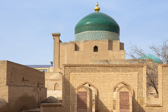 Pahlavan Mahmud Mausoleum with green tiled dome in Ichan Kala, Khiva. Historic brick architecture and carved inscriptions surround the main structure. Ideal for travel guides, cultural publications.