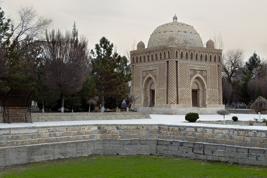 Ismail Samani Mausoleum in Bukhara surrounded by trees on an overcast winter day. Historic brick tomb with intricate patterns and a dome, ideal for travel and heritage publications.