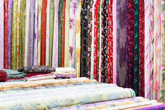 Colorful fabric bolts displayed at an oriental bazaar in Bukhara, Uzbekistan. Rolls of silk, brocade, and embroidered textiles hang vertically in a vibrant market stall. Ideal for travel, culture.
