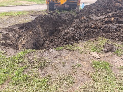 Deep earthen pit and a large pile of excavated soil on a lawn during municipal utility repair works.
