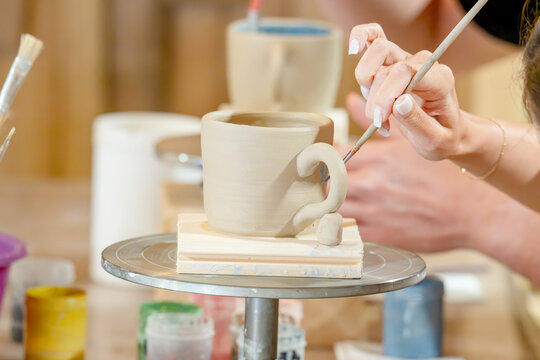 A woman steadily glazes a white ceramic mug on a rotating tray in a pottery studio;