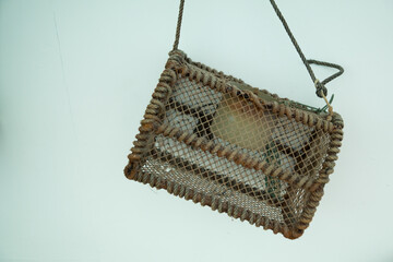 A rustic handmade fishing cage reinforced with thick brown rope, used for commercial or artisanal trapping of seafood, hanging on a white wall. © Phoscar