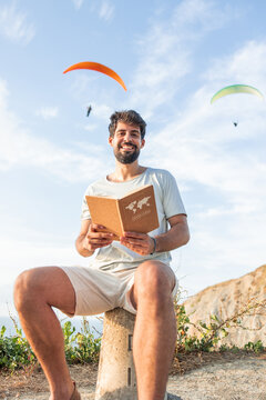 vertical Young man holding travel journal dreaming of paragliding adventure