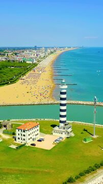 Vertical video. Italy, Jesolo. The 48-metre striped Piave Vecchia lighthouse, cylindrical tower with black and white horizontal bands, aerial drone view over the Sile River mouth and Adriatic coastli
