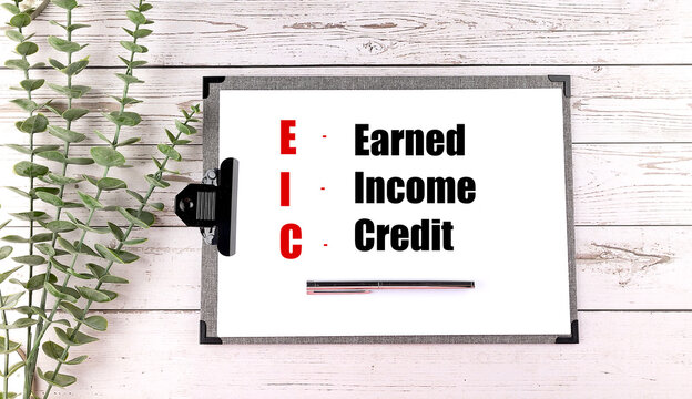 Earned income credit eic acronym on clipboard with pen and green leaves on wooden background representing tax benefits