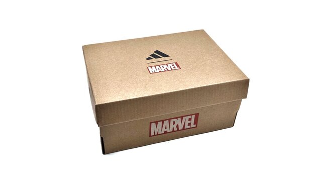 Photo of an Adidas kraft cardboard shoebox featuring the iconic black three-stripe logo alongside the red and white Marvel logo. 