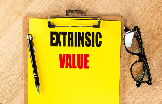 Extrinsic value concept on clipboard with pen and eyeglasses on wooden desk representing finance motivation psychology