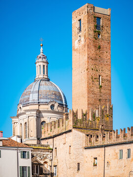 Mantova historic cityscape displaying an iconic view of the ancient Torre della Gabbia brick tower standing next to the ornate dome of the Basilica di Sant'Andrea against a clear blue sky